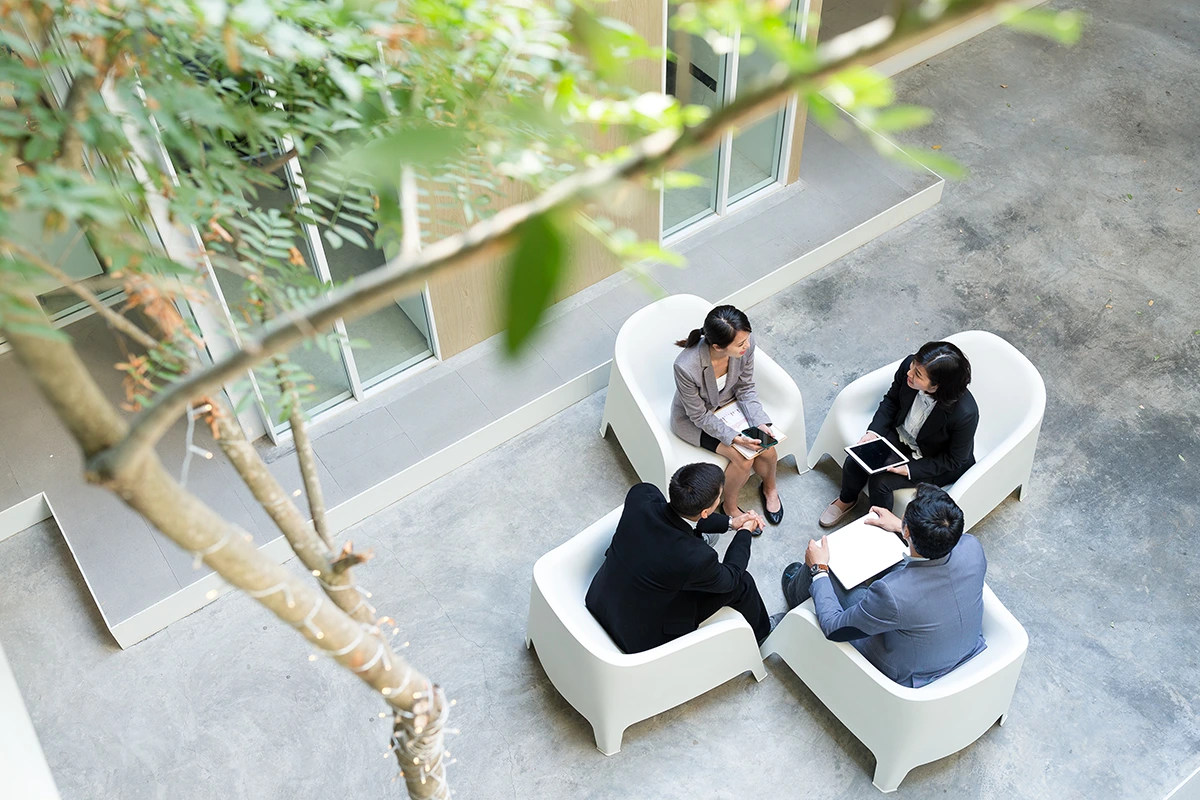 Vier Berufstätige sitzen im Kreis und besprechen sich in einem modernen Büro-Innenhof
