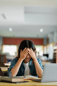 Überforderte Studentin zwischen Büchern und Laptop – Symbolbild für Leistungsdruck und Prüfungsangst